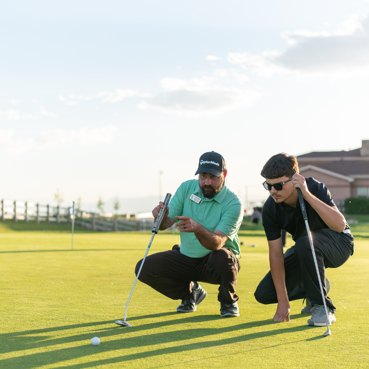 Two men kneel down on a golf course. 
