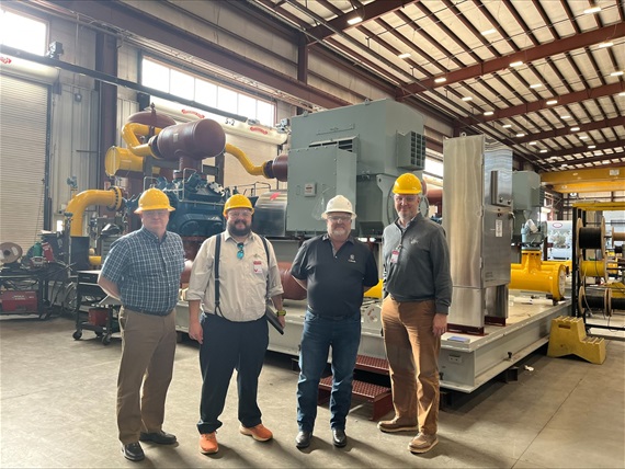 Four men in hardhats stand in an industrial building. 