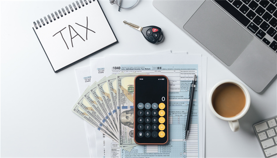 Calculator, money, coffee, computer, and tax documents on a desk. 